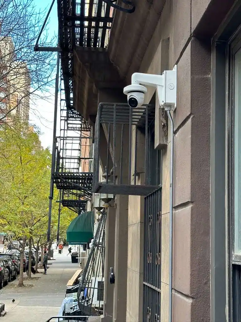 PTZ dome camera mounted on a NYC stone building exterior with fire escapes visible