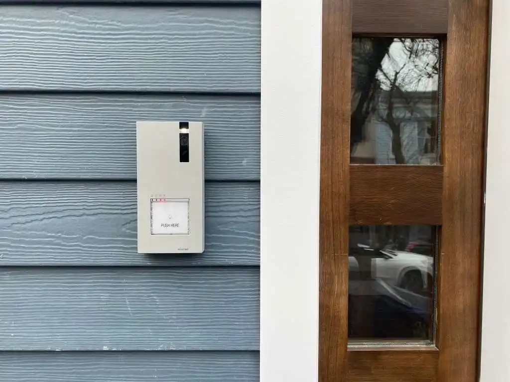 Video doorbell mounted on blue residential siding next to a wood front door