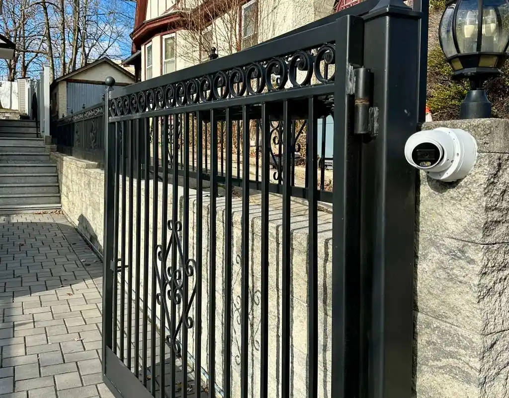 White bullet camera mounted on a stone pillar beside a wrought-iron residential gate
