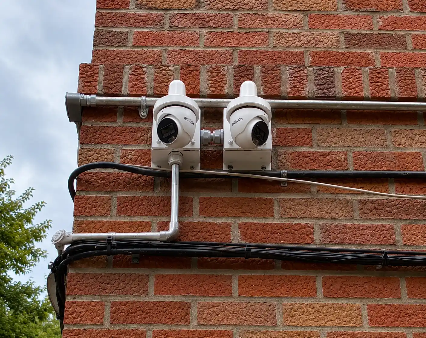 Two white security cameras mounted on conduit against a brick wall